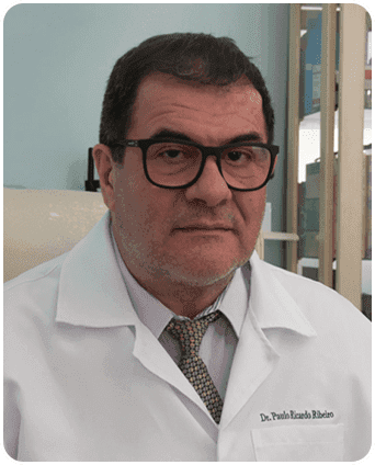 Dr. Paulo Ribeiro, homem branco, com cabelo escuro, utilizando um óculos preto e vestindo um jaleco branco.